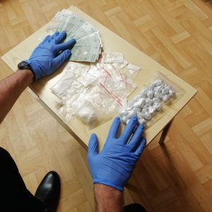 ręce policjanta w rękawiczkach i rozłożone na stoliku narkotyki