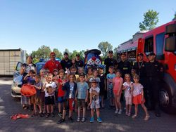 zdjęcie grupowe dzieci z policjantem, strażakami, ratownikiem wodnym i Sznupkiem przy wozie strażackim