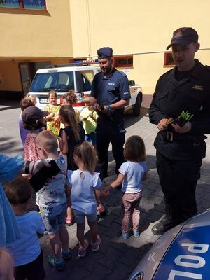 policjant i strażak rozdają dzieciom opaski odblaksowe