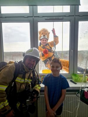 na zdjęciu strażak z dzieckiem w szpitalu a za oknem alpinista w przebraniu