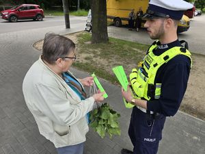na zdjęciu policjant wręcza kobiecie opaskę odblaskową