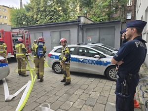 na zdjęciu policjanci i strażacy rozwijający węże