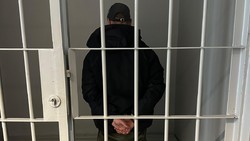 Zdjęcie przedstawia zatrzymanego mężczyznę, który stoi w pomieszczeniu z metalową kratą.