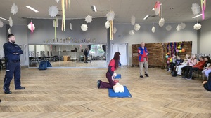 Na zdjęciu widać policjanta oraz ratownika WOPR, który pokazuje dzieciom jak udzielać pierwszej pomocy