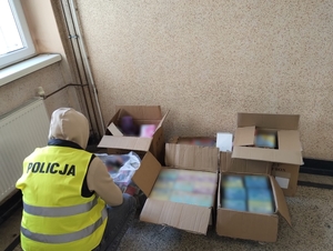 Zdjęcie przedstawia policjanta kucającego przed zabezpieczonym towarem bez polskich znaków akcyzy