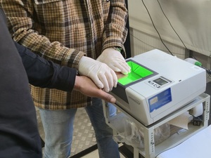 Na zdjęciu widać nieumundurowanego policjanta, który pobiera od zatrzymanego ślady daktyloskopijne