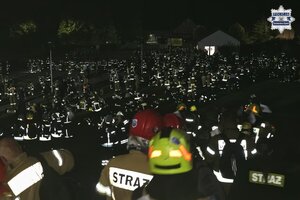 Na zdjęciu widocznych jest kilkudziesięciu strażaków w zacienionej scenerii.