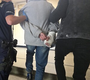 Na zdjęciu widocznych jest dwóch policjantów doprowadzających osobę zatrzymaną
