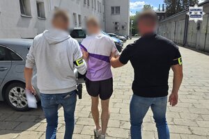 Na zdjęciu widocznych jest dwóch nieumundurowanych policjantów w trakcie doprowadzenia osoby zatrzymanej