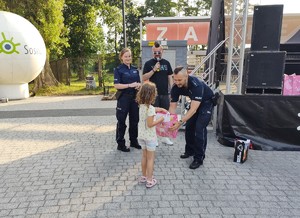 Zdjęcie przedstawia umundurowanych policjantów wręczających dziecku nagrodę