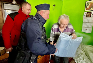 Zdjęcie przedstawia umundurowanych policjantów oraz księdza wręczających paczkę osobie potrzebującej.