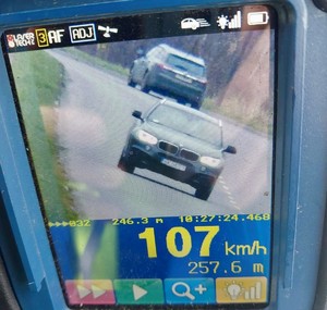 Zdjęcie przedstawia samochód poruszający się po drodze. Na dole napis &quot;107 km/h&quot;.