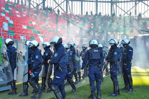 Zdjęcie przedstawia umundurowanych policjantów na terenie stadionu.