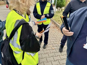 Zdjęcie przedstawia uczennice w kamizelkach odblaskowych wręczające elementy odblaskowe.