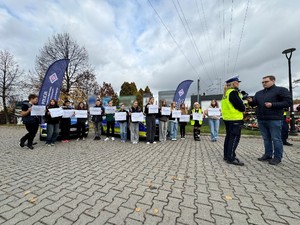 Zdjęcie przedstawia grupę dzieci oraz umundurowaną policjantkę udzielającą informacji mediom.