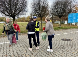 Zdjęcie przedstawia umundurowaną policjantkę wręczającą ludziom opaski odblaskowe.