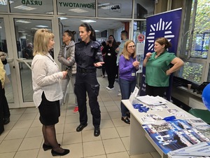 Zdjęcie przedstawia umundurowaną policjantkę rozmawiającą z uczestnikami wydarzenia.