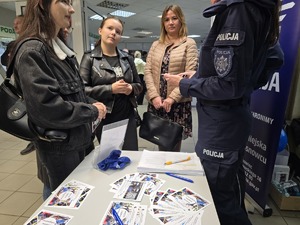 Zdjęcie przedstawia umundurowanych policjantów oraz uczestników. W tle ulotki zachęcające do służby w Policji.