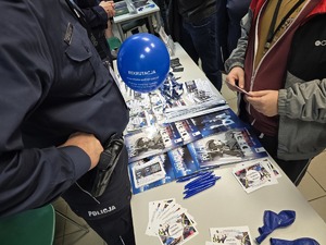 Zdjęcie przedstawia umundurowanych policjantów oraz uczestników. W tle ulotki zachęcające do służby w Policji.
