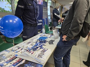 Zdjęcie przedstawia umundurowanych policjantów oraz uczestników. W tle ulotki zachęcające do służby w Policji.