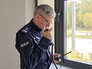 Zdjęcie przedstawia umundurowanego policjanta rozmawiającego przez radiostację.