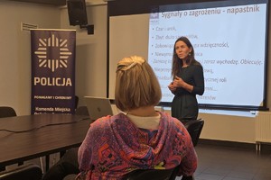 Zdjęcie przedstawia psycholog policyjną rozmawiającą z uczestniczkami kursu w sali.