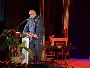 Zdjęcie przedstawia umundurowanego policjanta przemawiającego do uczestników ze sceny.