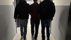 Zdjęcie przedstawia dwóch nieumundurowanych policjantów oraz zatrzymanego mężczyznę.