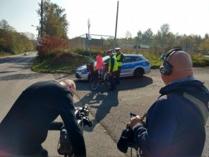 Ekipa z TVP1 w trakcie nagrania. w tle Policjanci z Wydziału Ruchu Drogowego KMP Świętochłowice podczas kontroli rowerzystki.