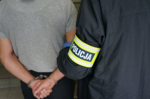 na zdjęciu zatrzymany mężczyzna, zakuty w kajdanki w asyście policjanta z wydziału kryminalnego