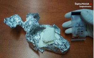 zabezpieczony zwitek foli aluminiowej z białą substancją proszkową obok tester narkotykowy pokazujący obecność amfetaminy