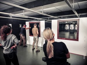 Na zdjęciu nieumundurowane policjantki przyglądają się ćwiczeniu wykonywanemu przez instruktorów polegającym na oddaniu strzału do tarczy z broni krótkiej zza przesłony