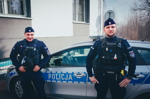 Na zdjęciu dwaj świętochłowiccy stróże prawa w umundurowaniu ćwiczebnym Sierżant sztabowy Dawid Michalik i sierżant Seweryn Ogrocki. W tle za nimi widać policyjny radiowóz