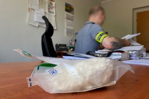 nieumundurowany policjant z opaską policja na ręce siedzi przy biurku, na pierwszym planie leżące na blacie worki z narkotykami