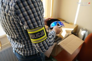 nieumundurowany policjant z opaską policja na ramieniu trzyma w ręku podrobione okulary jednej ze znanych firm sportowych