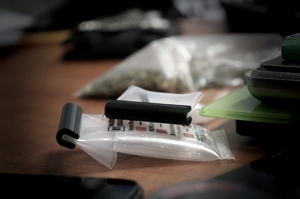 leżący na stole tester do narkotyków, w tle worek z marihuaną, z prawej strony waga elektroniczna