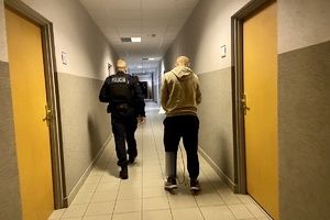 policjant prowadzący zatrzymanego mężczyznę po korytarzu