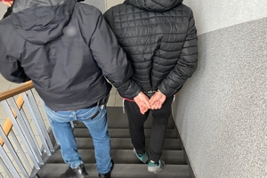 zdjęcie przedstawia: nieumundurowanego policjanta prowadzącego po schodach zatrzymanego mężczyznę