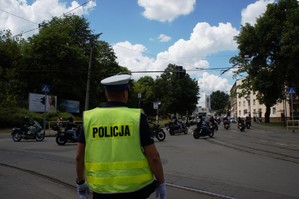zdjęcie przedstawia: policjanta kierującego ruchem, policyjny radiowóz oraz kolumna przejeżdżających motocykli