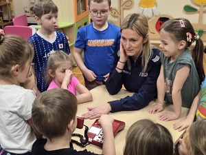 zdjęcie przedstawia policjantkę w przedszkolu i dzieci w okół niej przy telefonie