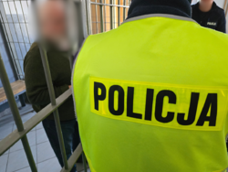 zdjęcie przedstawia mężczyznę za kratkami i policjantka w kamizelce odblaskowej