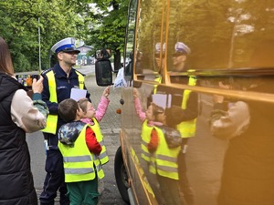 zdjęcie przedstawia policjantów z dziećmi ubranymi w kamizelki odblaskowe podczas akcji profilaktycznej wręczające laurki kierowcom