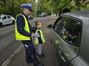 zdjęcie przedstawia policjantów z dziećmi ubranymi w kamizelki odblaskowe podczas akcji profilaktycznej wręczające laurki kierowcom
