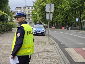 zdjęcie przedstawia policjanta na tle radiowozu
