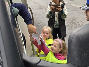 zdjęcie przedstawia policjantów z dziećmi ubranymi w kamizelki odblaskowe podczas akcji profilaktycznej wręczające laurki kierowcom