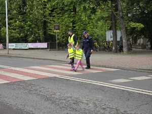 zdjęcie przedstawia policjantkę przechodzącą z dziećmi przez ulicę