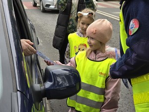 zdjęcie przedstawia policjantów z dziećmi ubranymi w kamizelki odblaskowe podczas akcji profilaktycznej wręczające laurki kierowcom
