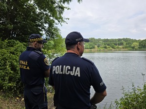 zdjęcie przedstawia policjanta i strażnika miejskiego nad stawem