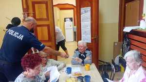 zdjęcie przedstawia policjanta wręczającego broszury seniorom