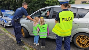 zdjęcie przedstawia: policjanta i dzieci z przedszkola wręczające kierowcy medal